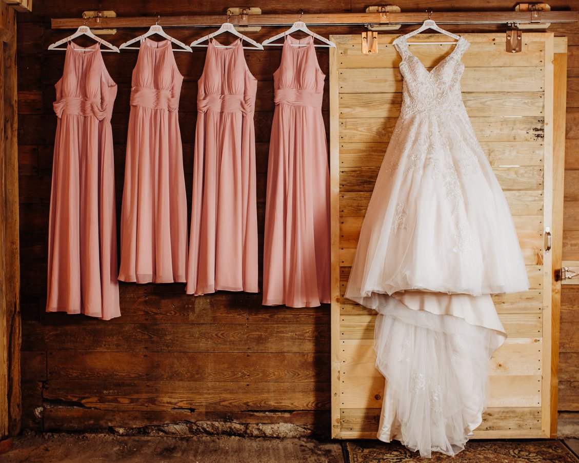 bridal gown and bridesmaids dresses hanging on barn door