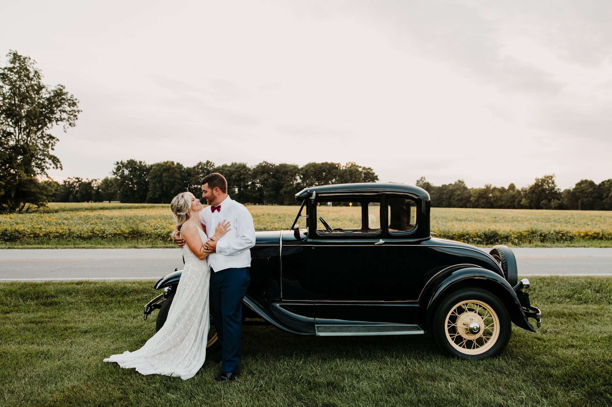 bride and groom embracing next to antique car