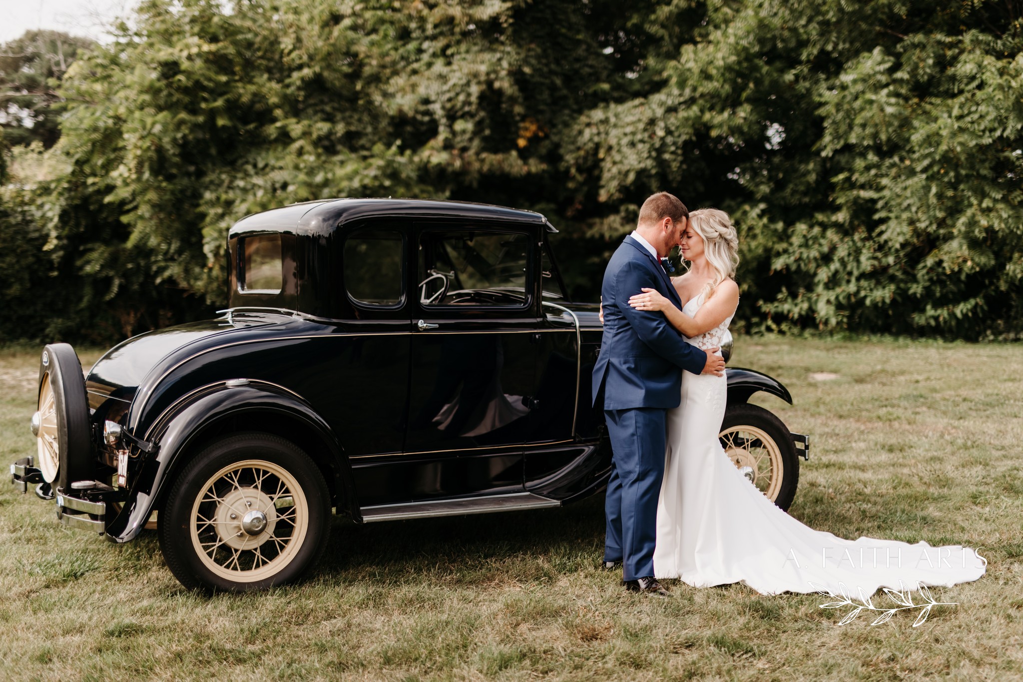 bride and groom embracing in front of antique car