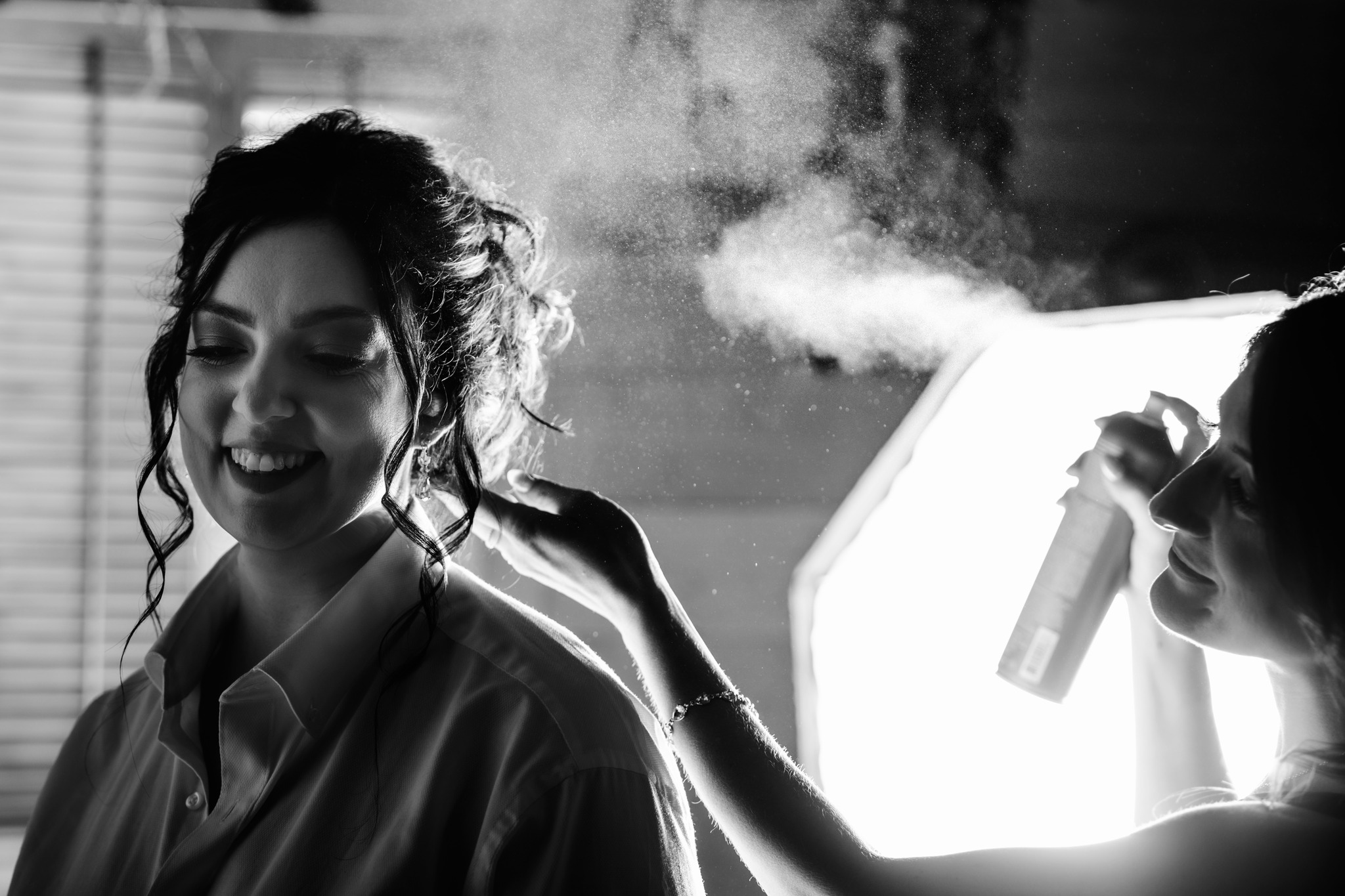 hair stylist spraying hair spray on bride's hair
