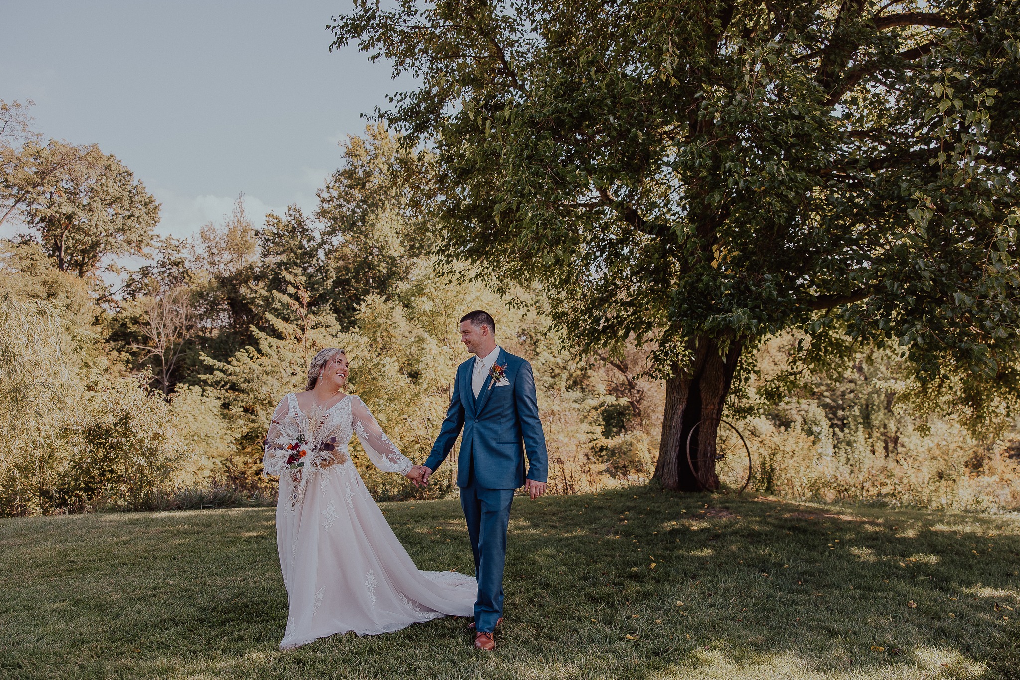 bride and groom holding hands while walking through green field