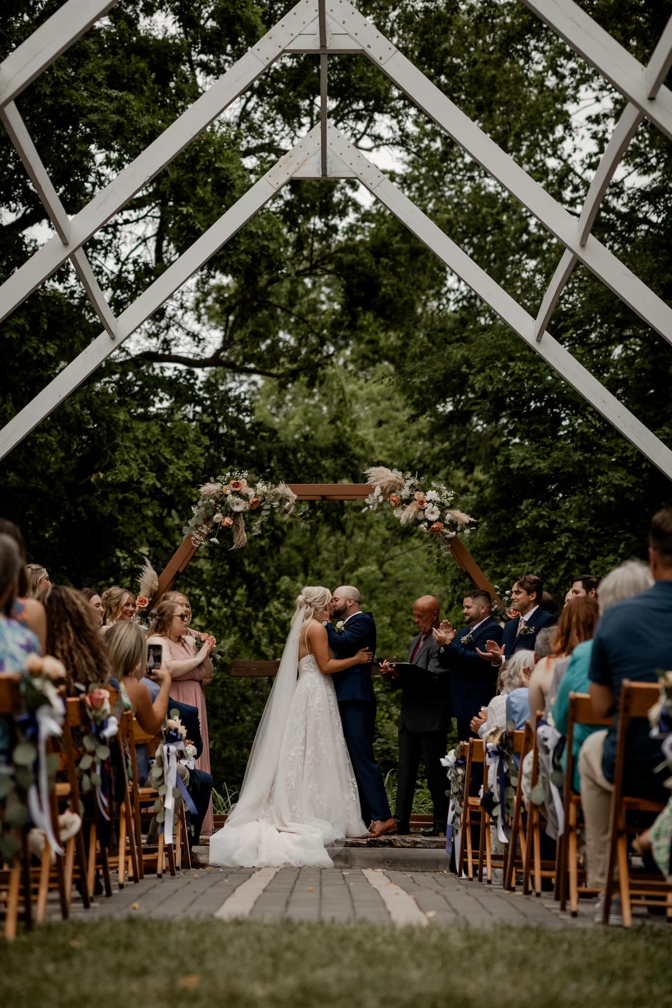 bride and groom's first kiss under white pergola